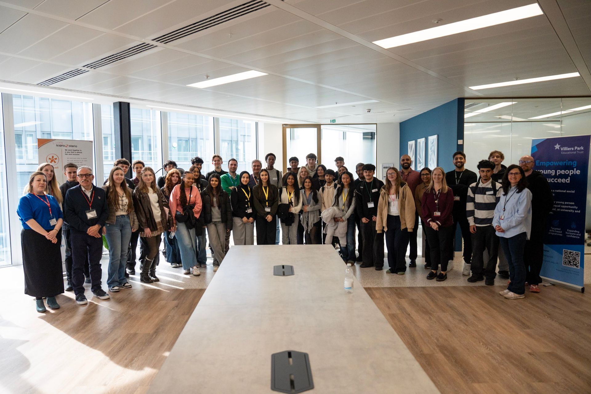 Group of people standing in a bright office conference room, posing beside a long table and blue banner.