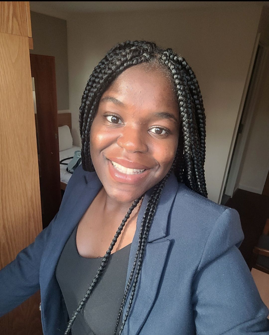 A woman with braids is smiling and wearing a blue jacket.