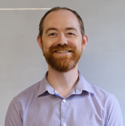 A man with a beard is smiling and wearing a purple shirt