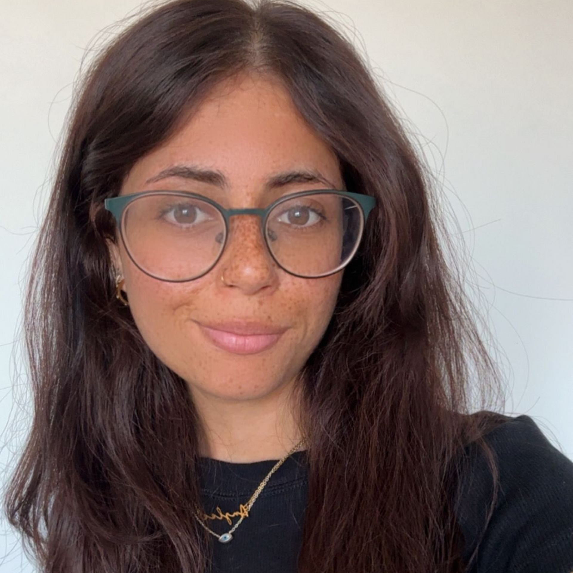 Close-up portrait of a person wearing glasses and a black top against a plain light background