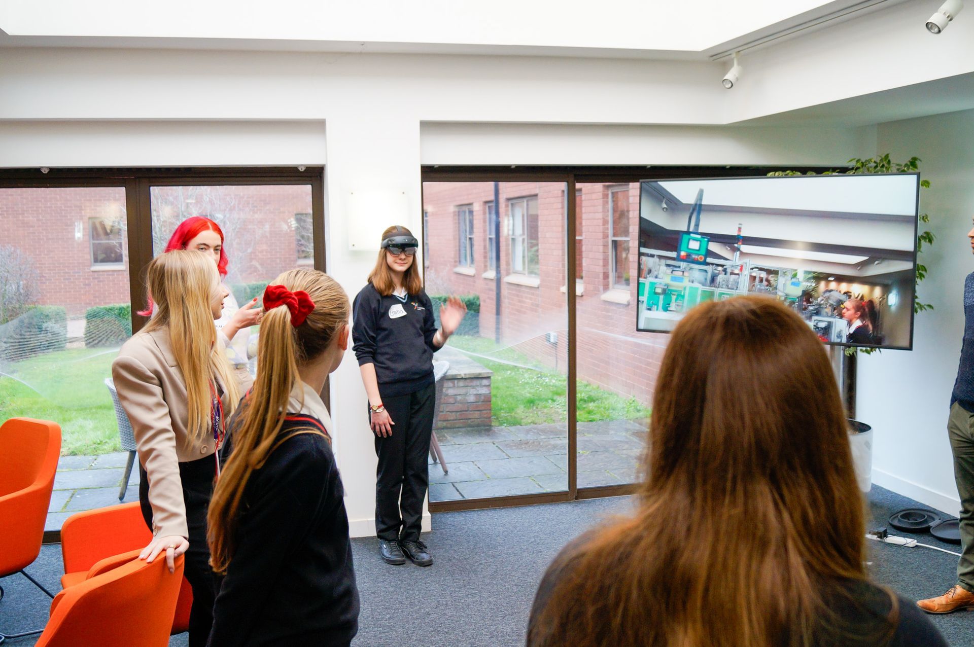 A group of people are standing in a room in front of a large window.