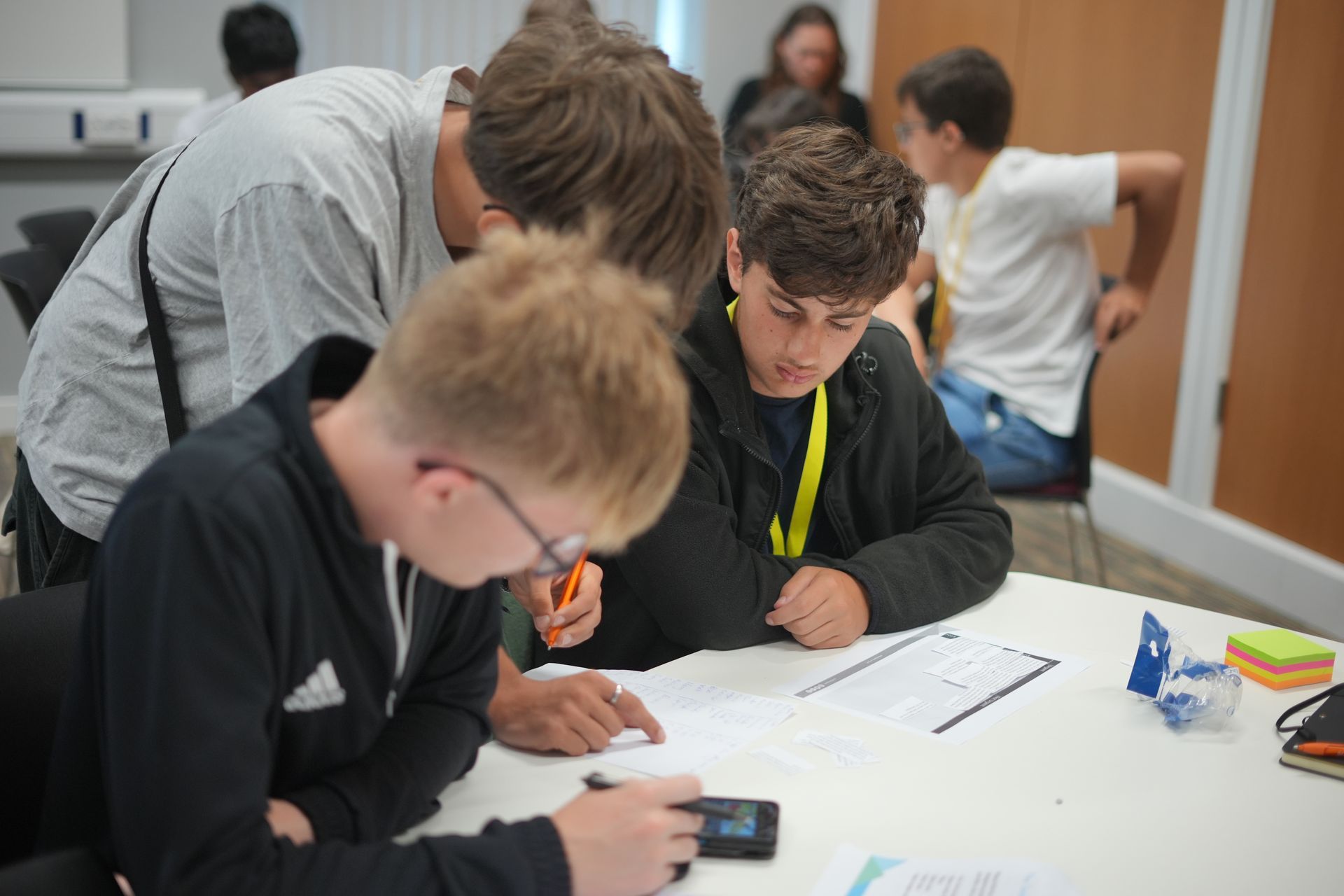 A group of young men are sitting at a table looking at a piece of paper.