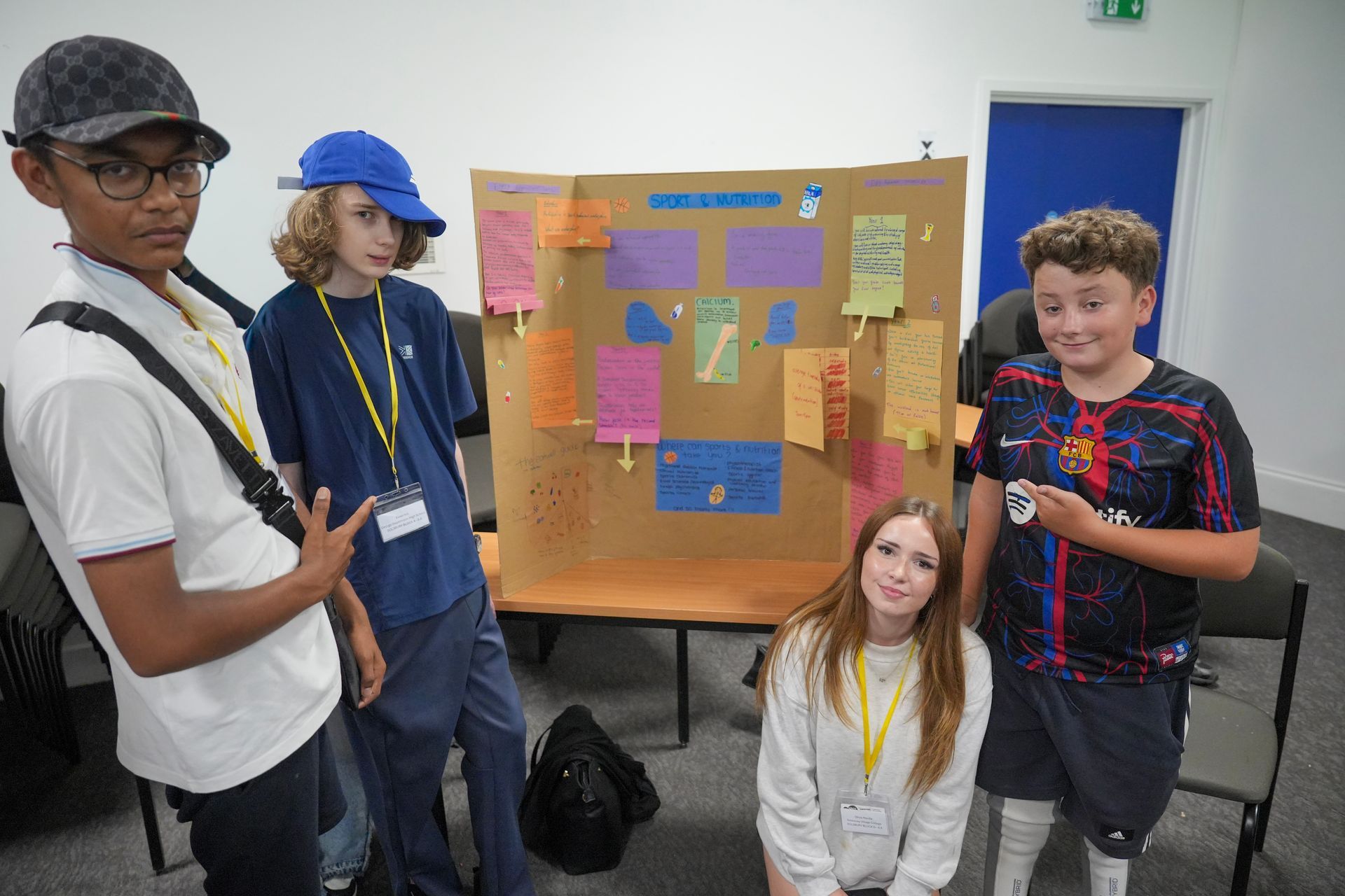 Four students posing beside a poster board with colorful notes in a classroom.