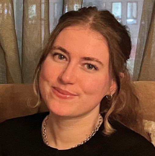 A woman is sitting on a couch wearing a black shirt and a necklace.