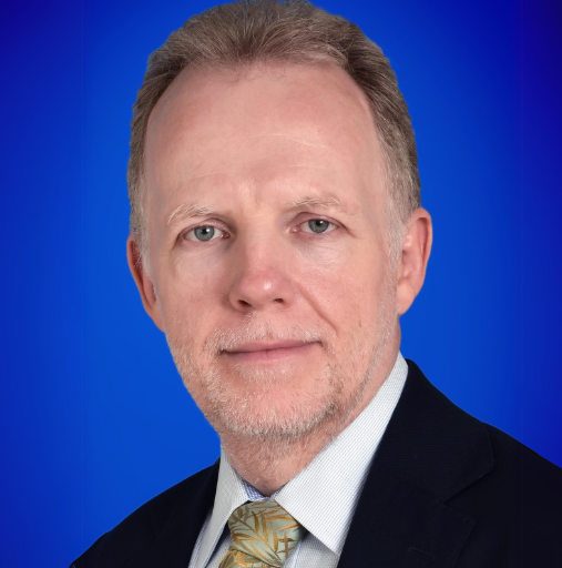 A man in a suit and tie is standing in front of a blue background.