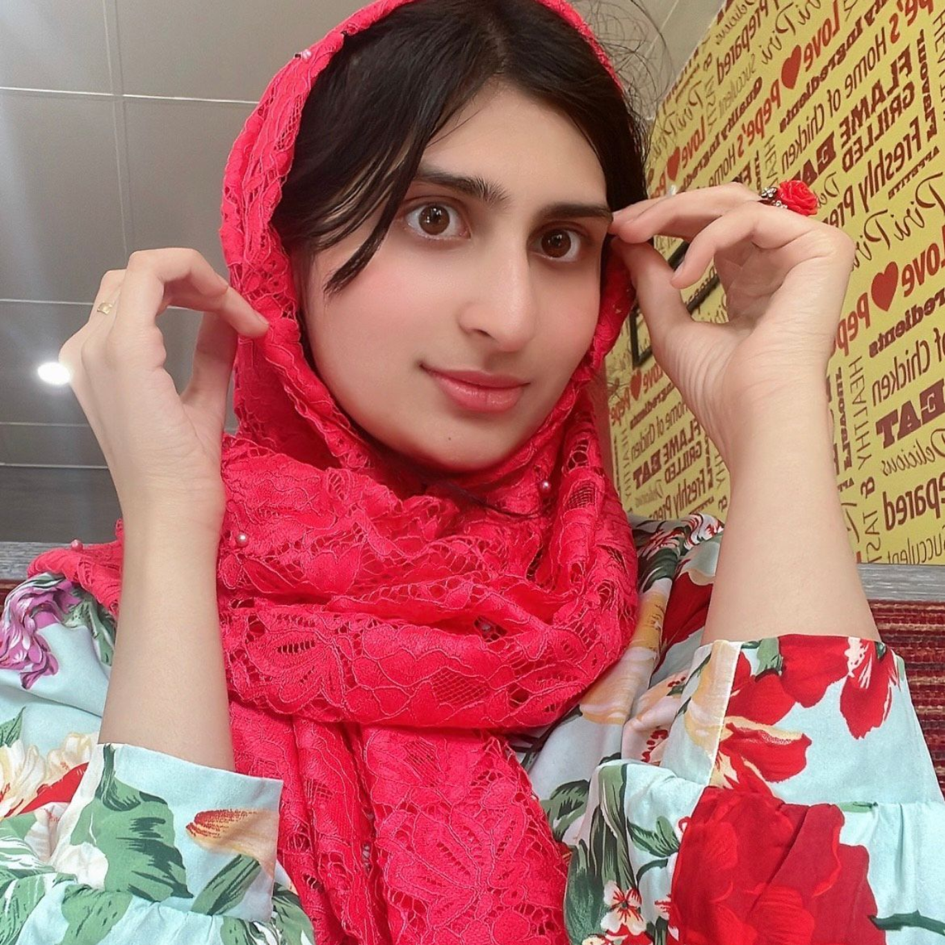 Man in vest and tie stands outside near greenery and a brick building.