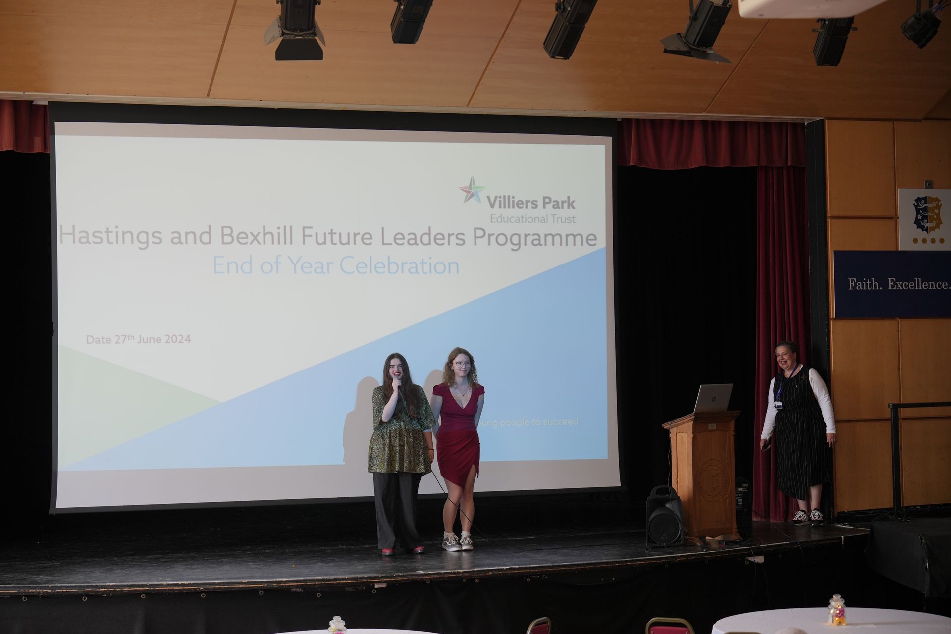 Three women are standing on a stage in front of a large screen that says leaders programme