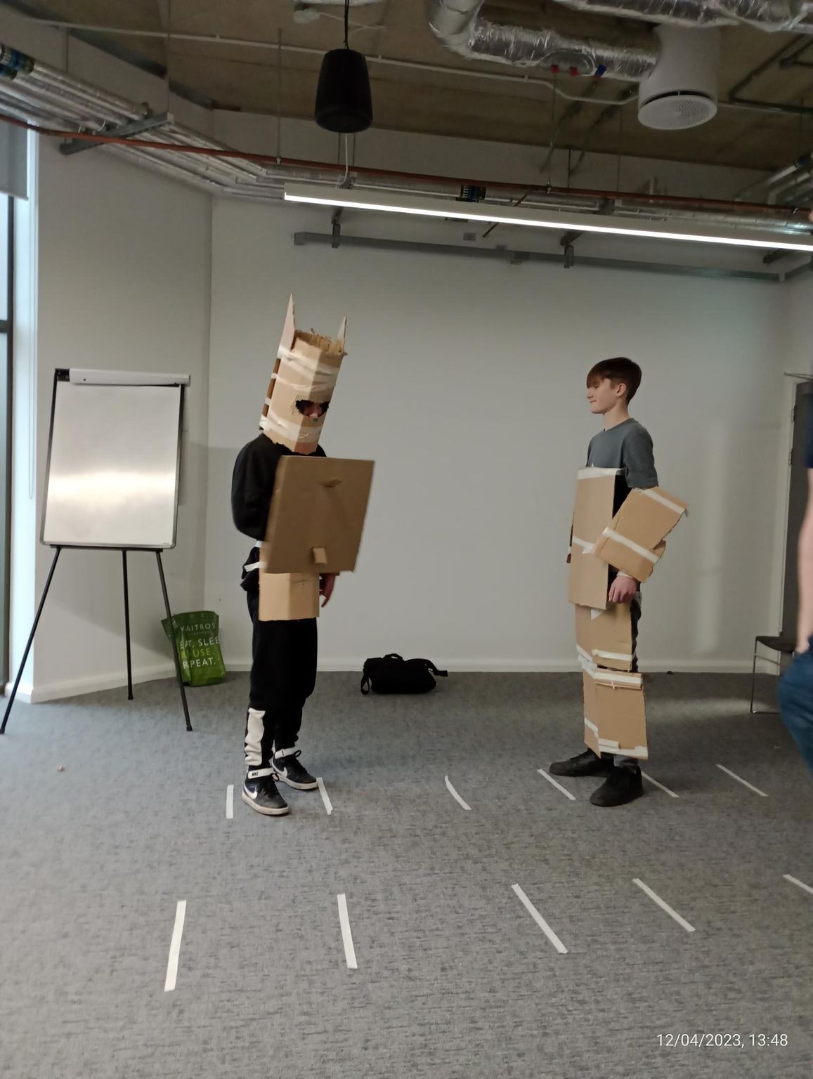 Two people are standing in a room with cardboard boxes on their heads.