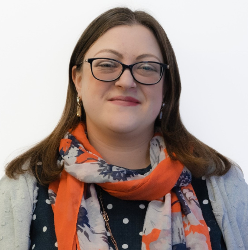 A woman wearing glasses and an orange scarf smiles for the camera