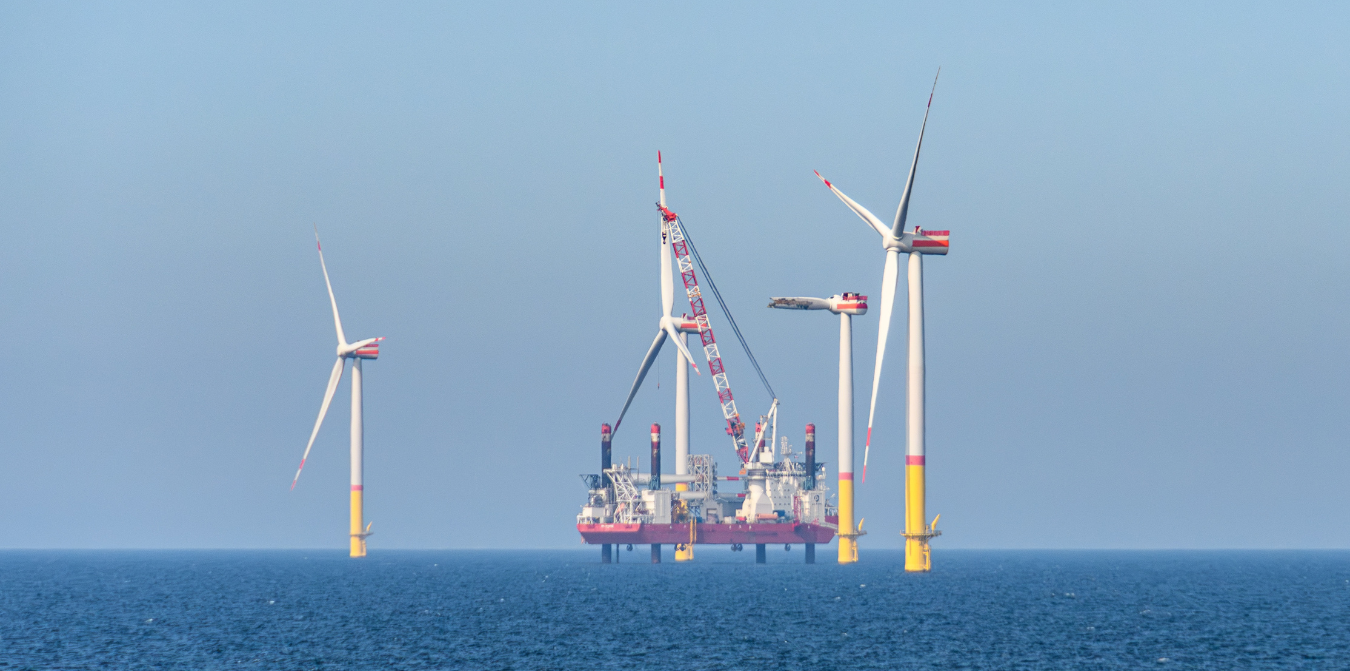 Offshore wind turbines with a construction platform in the ocean under a clear blue sky.