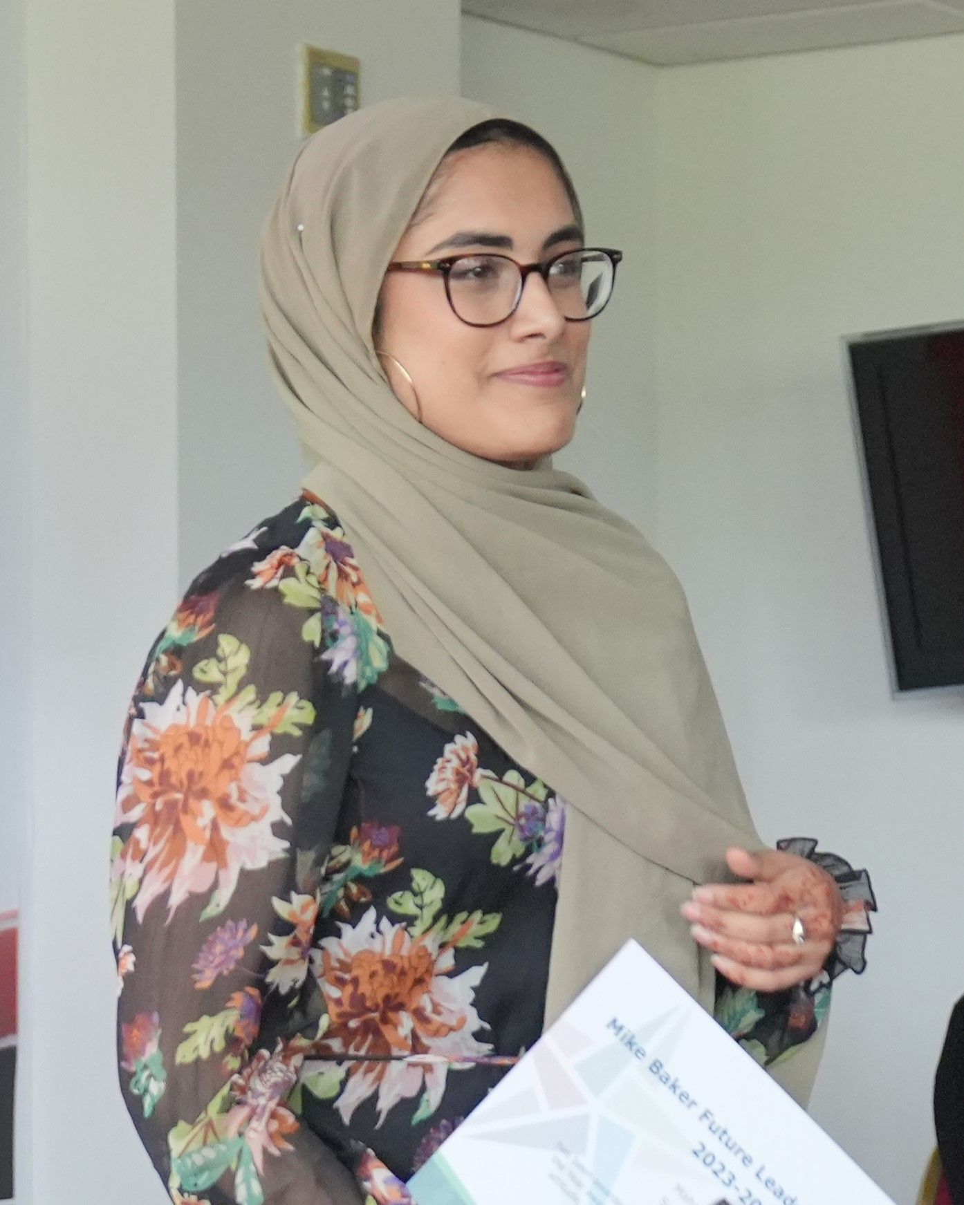 A woman wearing a hijab and glasses is holding a certificate