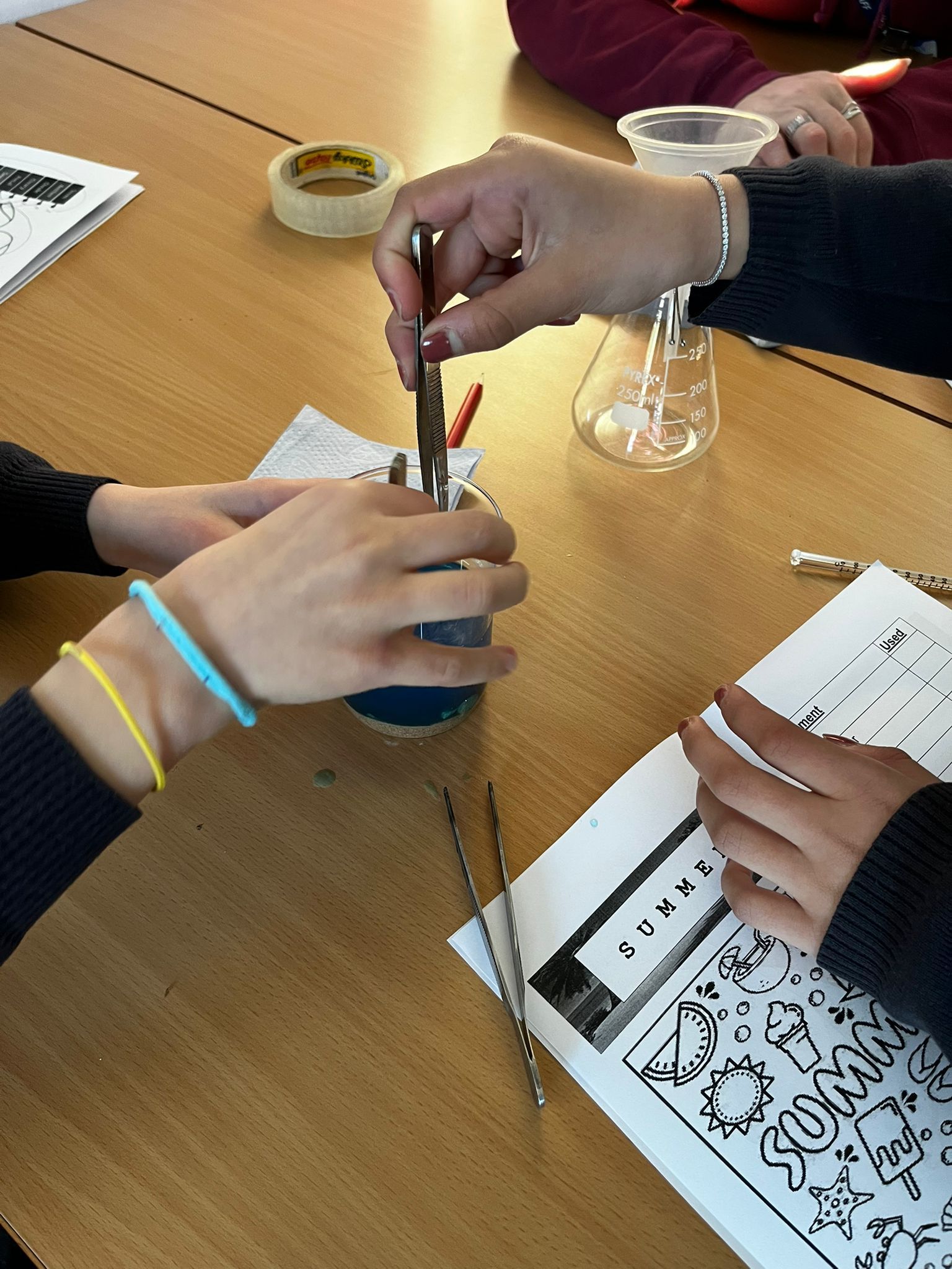 Hands using pipettes over a beaker during a tabletop science experiment