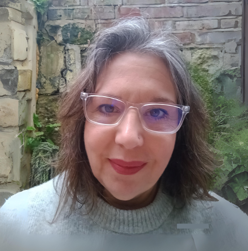 A woman wearing glasses and a sweater is standing in front of a brick wall.