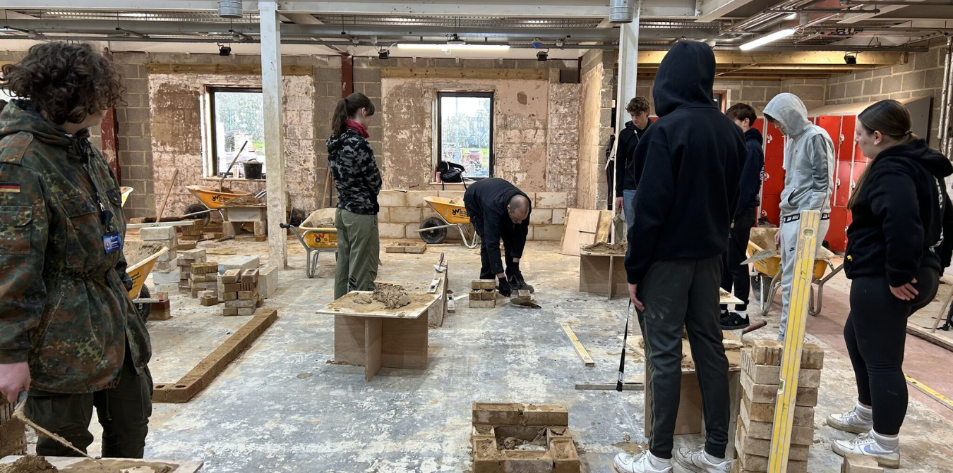 Students in a construction workshop observing a bricklaying demonstration.