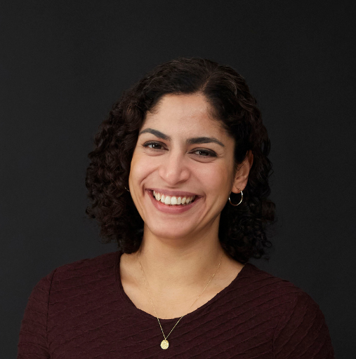 A woman with curly hair is smiling and wearing a necklace