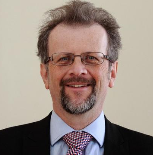 A man wearing glasses and a tie smiles for the camera