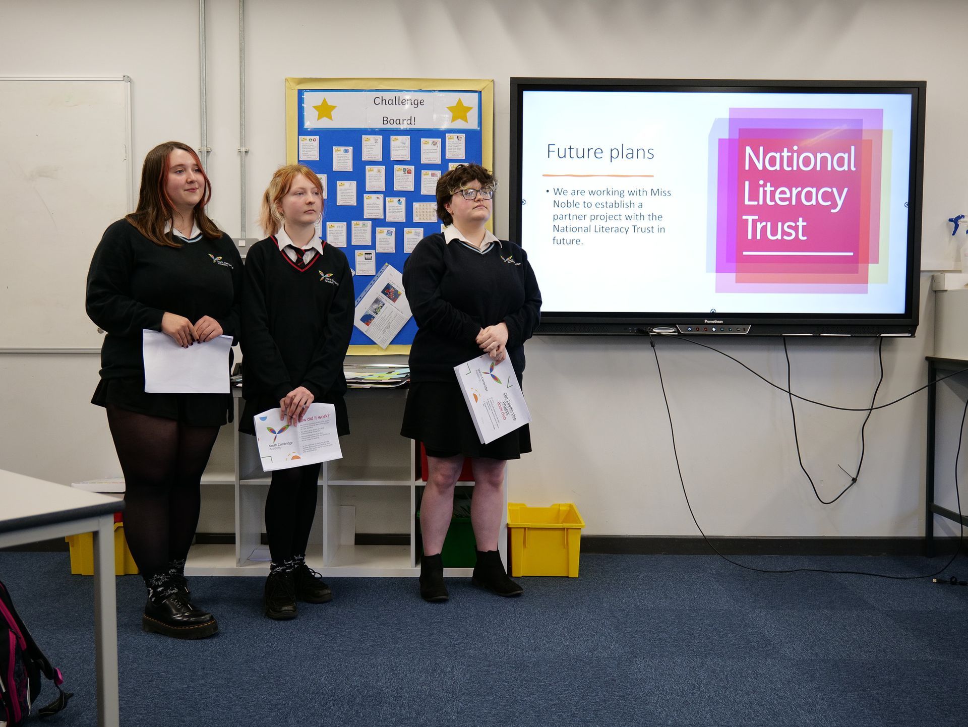 Three girls are standing in front of a screen that says national literacy trust