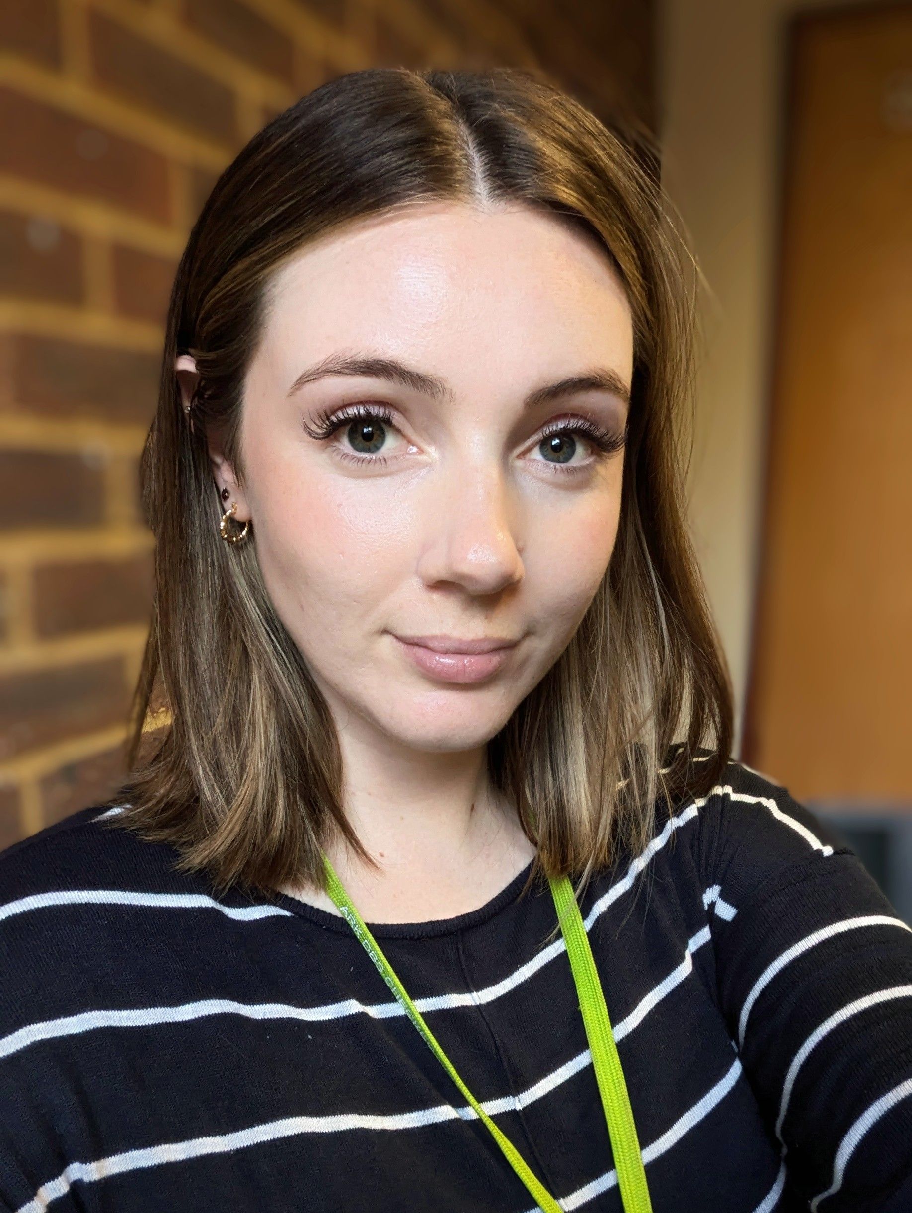 A woman in a striped shirt is taking a selfie in front of a brick wall.