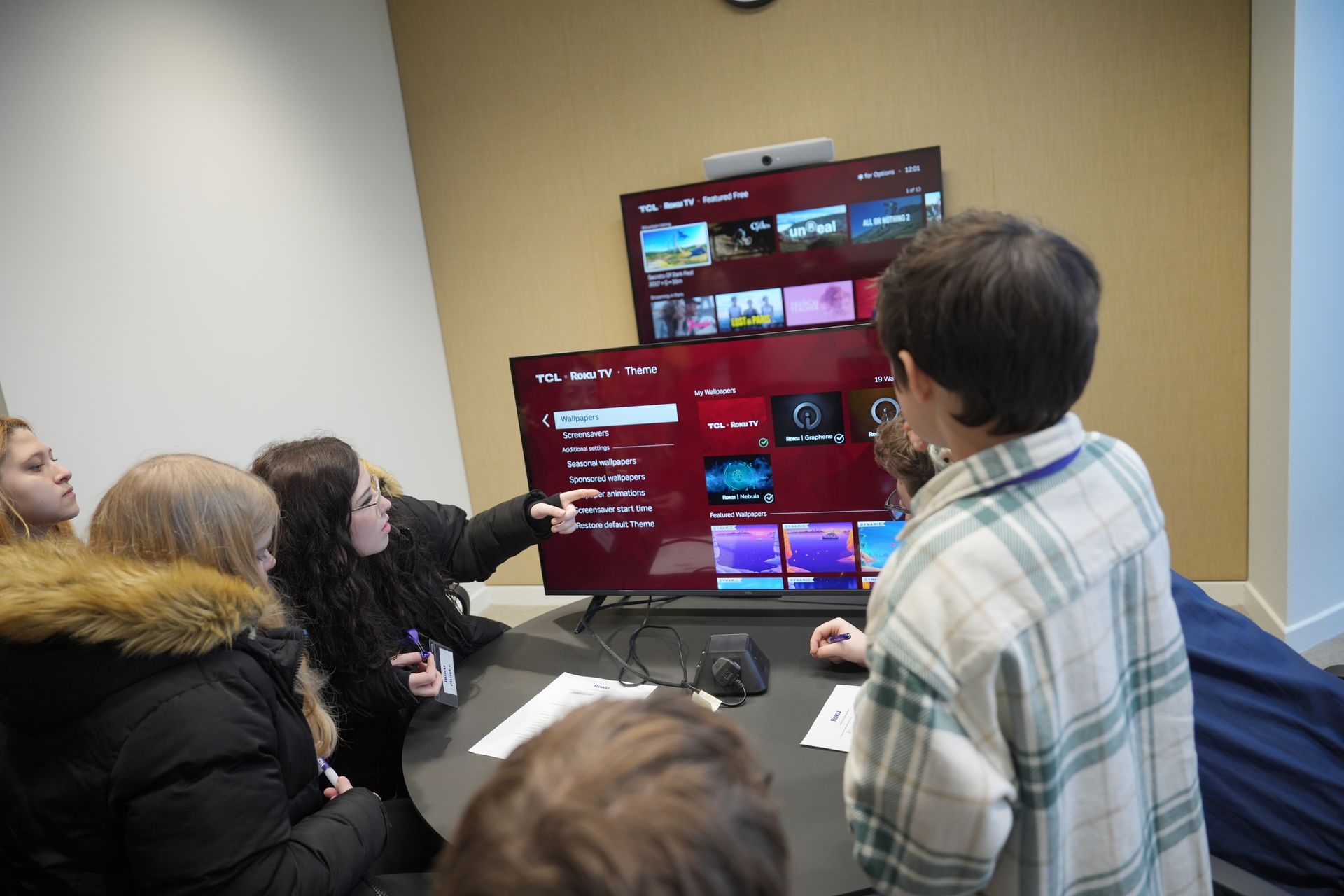 A group of people are sitting around a table looking at a television.
