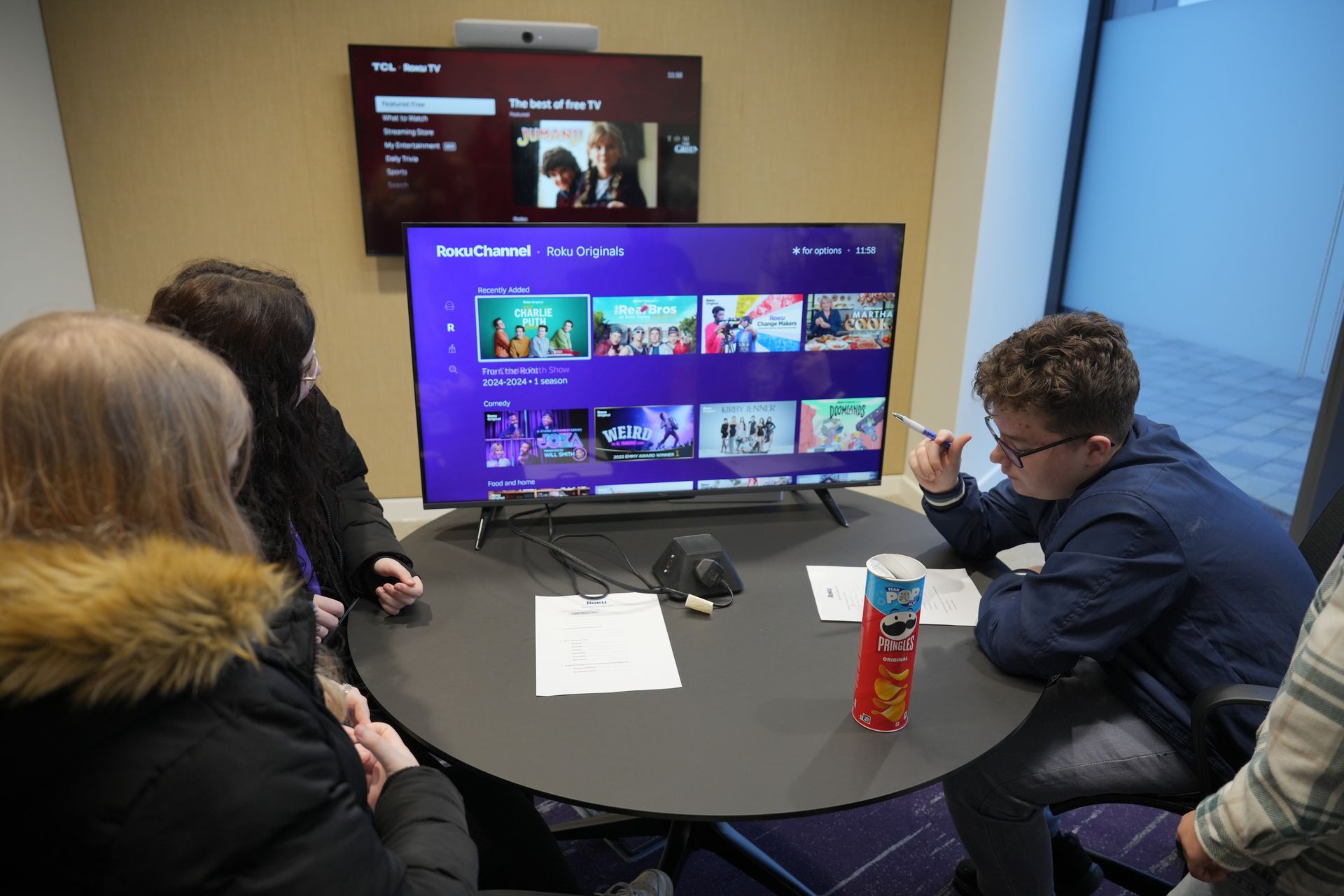 A group of people are sitting around a table looking at a television.