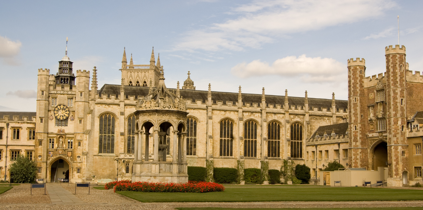 Exterior view of a large, ornate building with a clock tower and a green lawn in front.