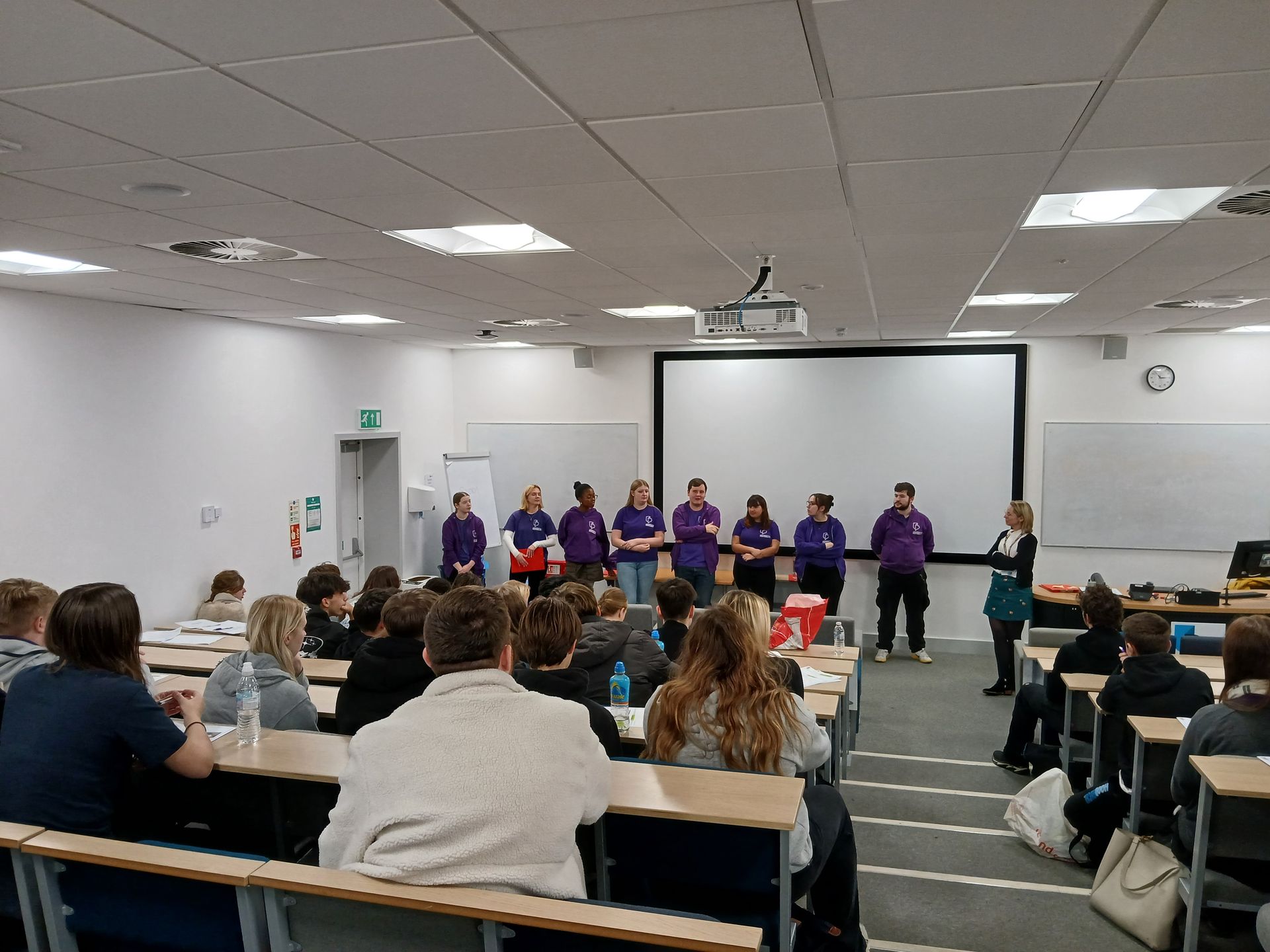 A group of people are standing in front of a large screen in a lecture hall.