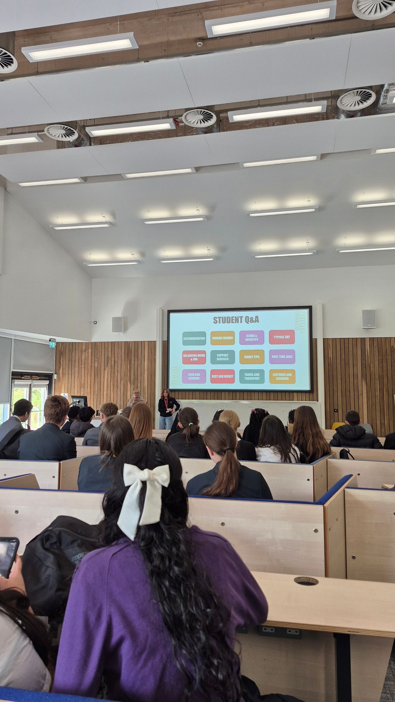 Audience seated in a lecture hall watching a presentation on a projector screen