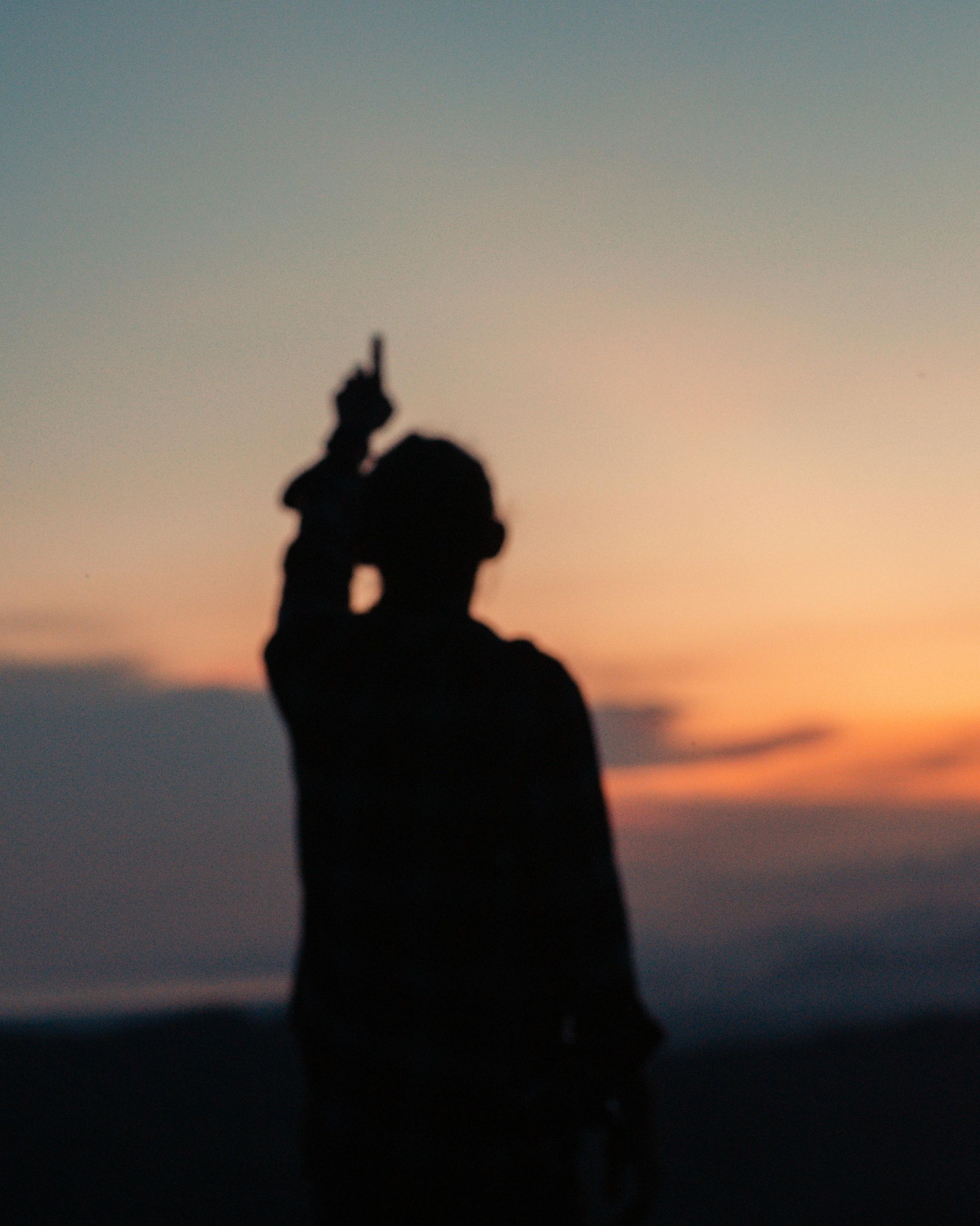 Silhouette of a person with an arm raised, pointing upward at a colorful sunset.