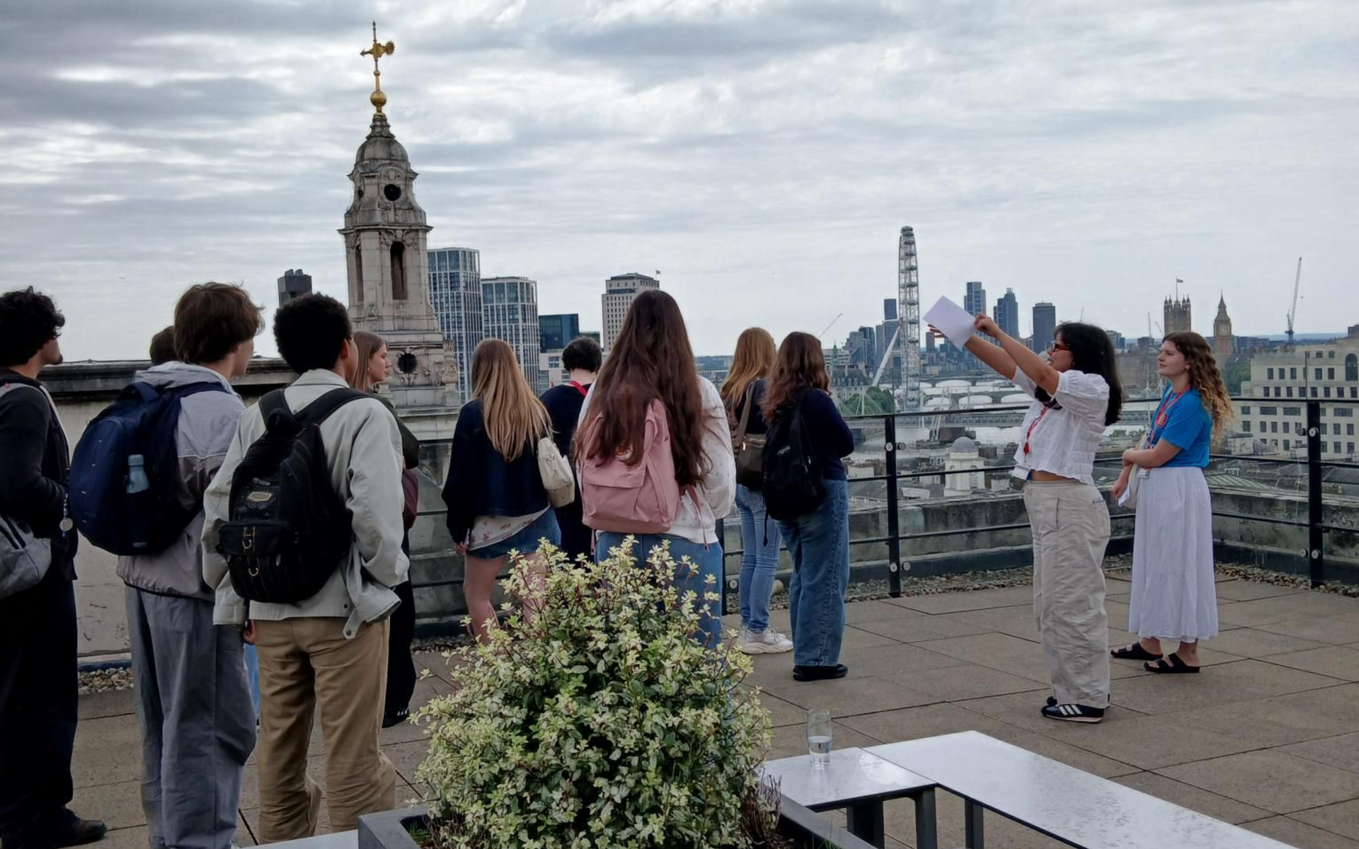 Students on a rooftop terrace overlooking London city skyline under cloudy skies