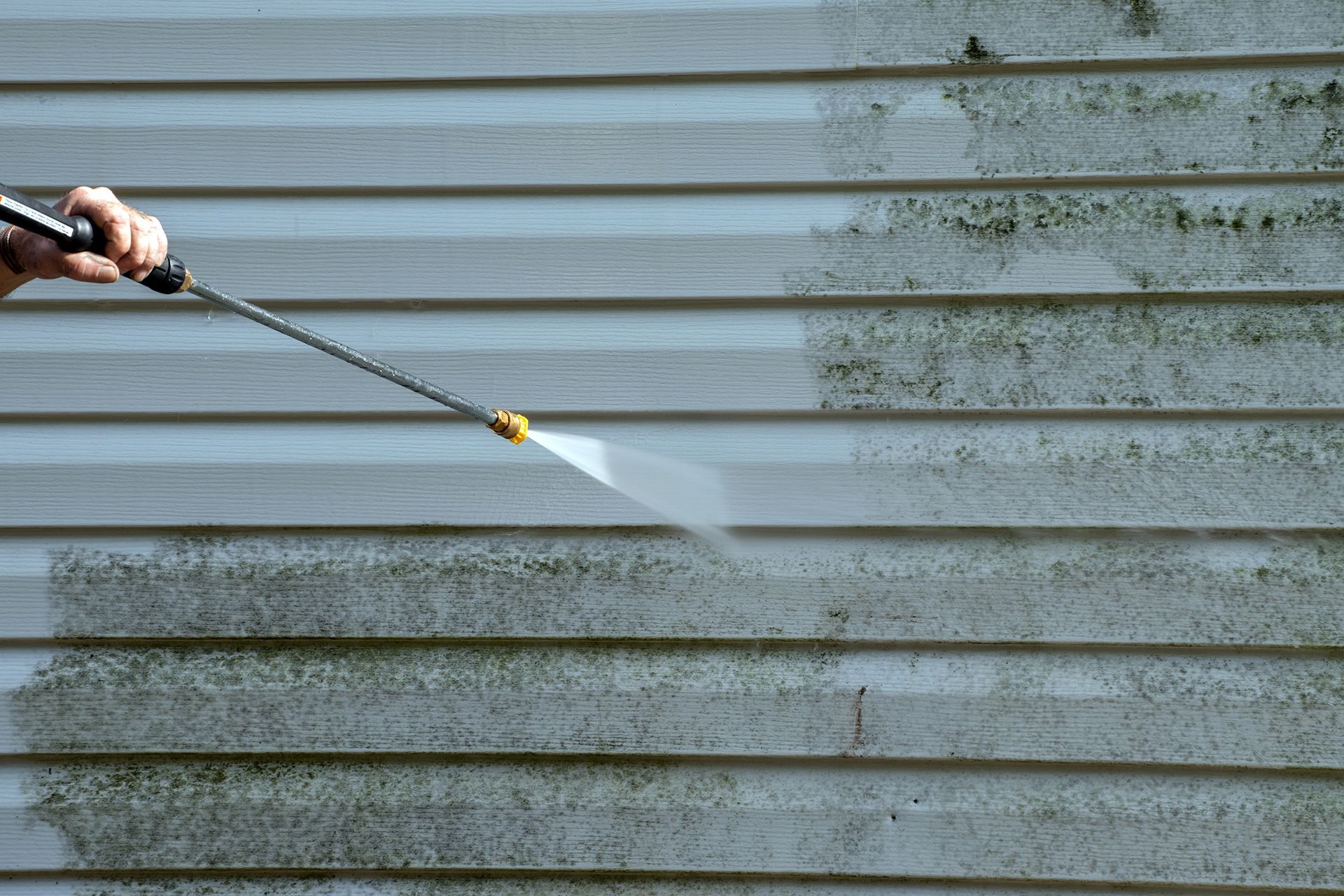 A person is cleaning a siding with a high pressure washer.
