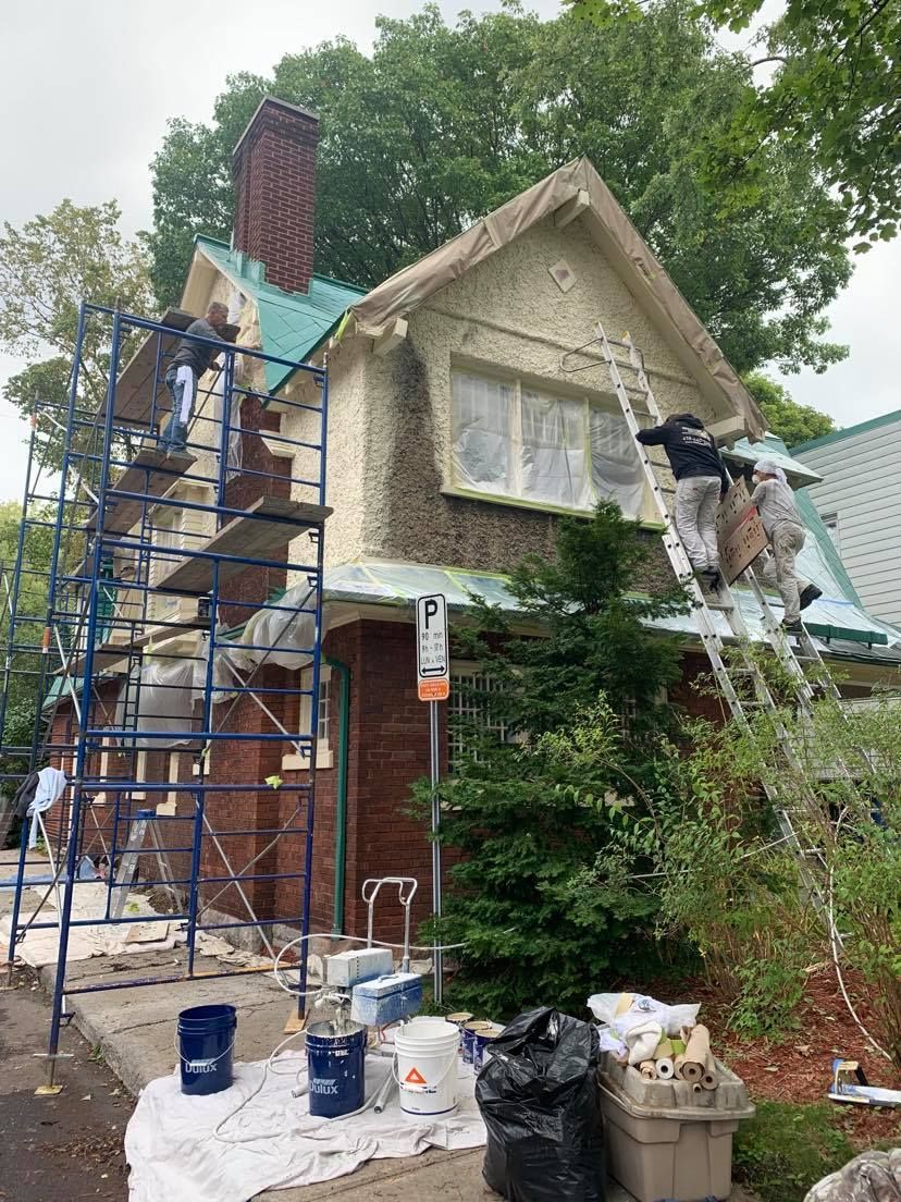 A man is standing on a ladder painting the side of a house.