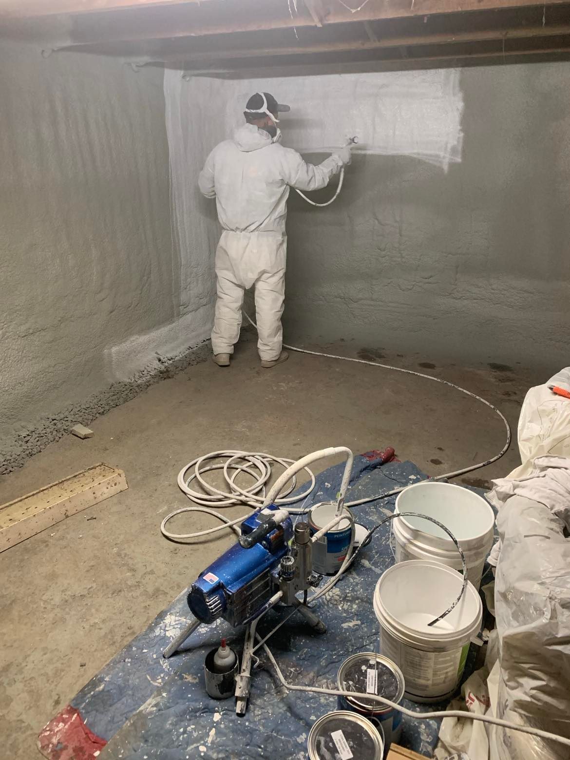 A man in a protective suit is painting a wall in a basement.