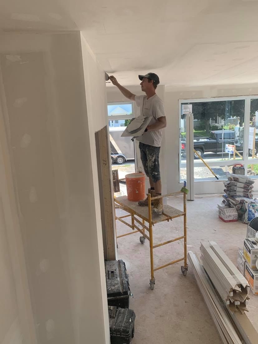 A man is standing on a scaffolding in a room painting a wall.