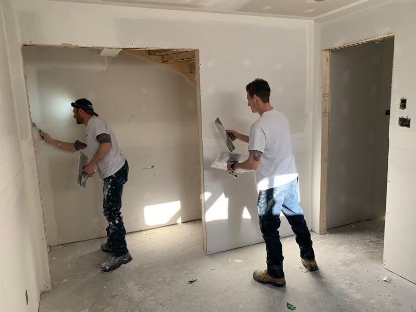 Two men are plastering a wall in a room.