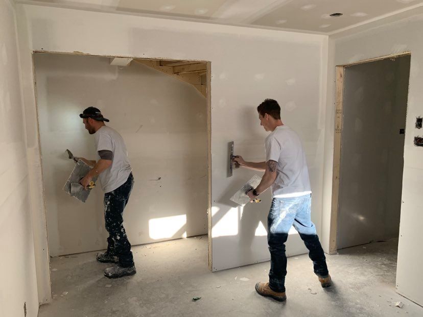 Two men are plastering a wall in a room.