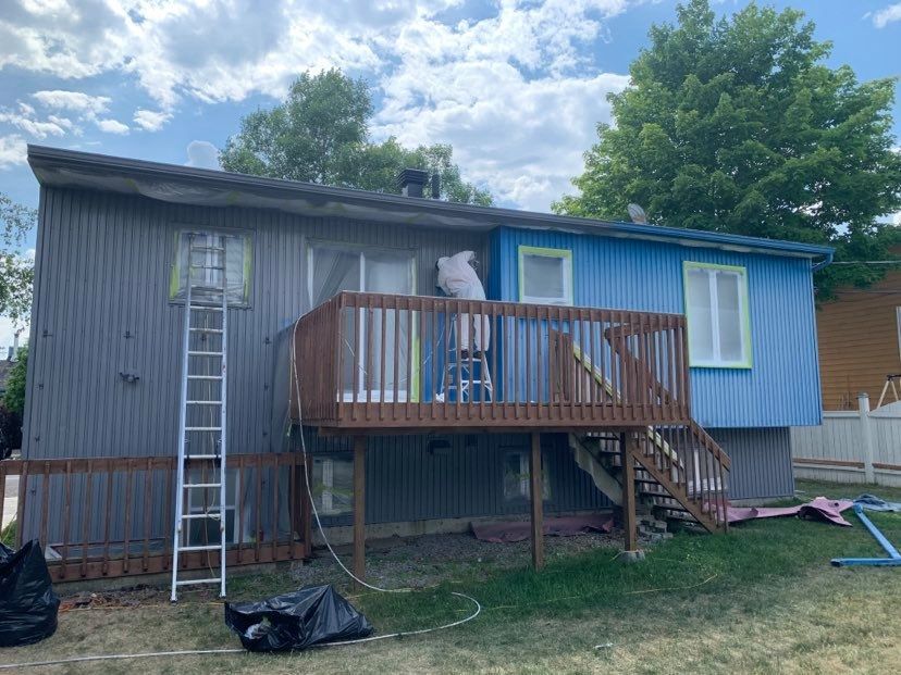 A man is painting the side of a blue house.