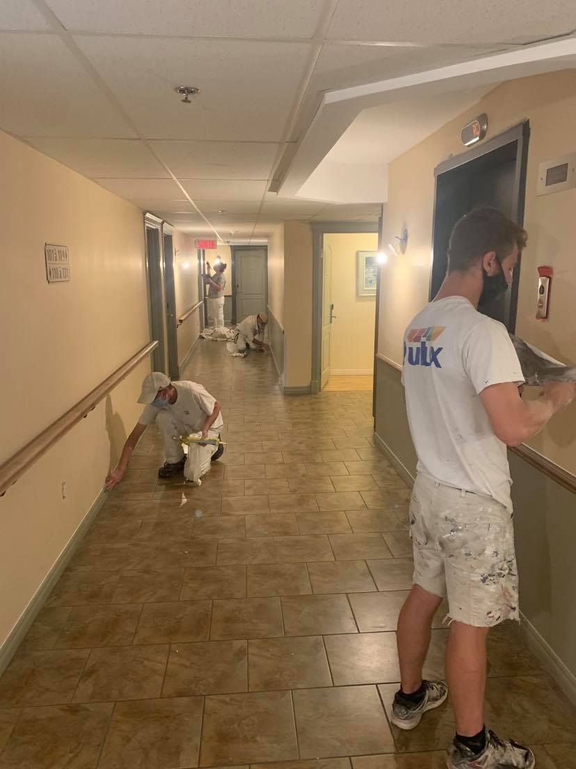 A man wearing a mask is standing in a hallway painting a wall.