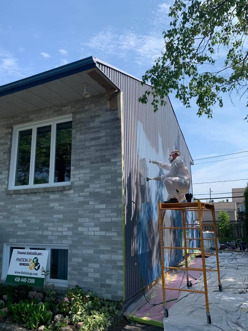 A man is standing on a ladder painting the side of a house.