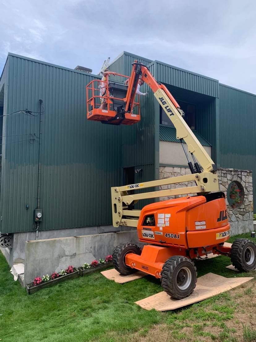 An orange crane is sitting in front of a green building.