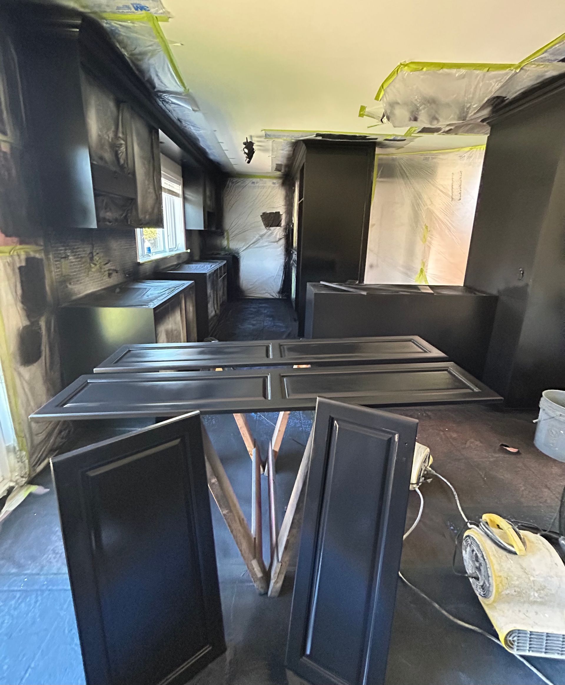 
Une cuisine avec des armoires noires en cours de peinture et une table au milieu de la pièce.