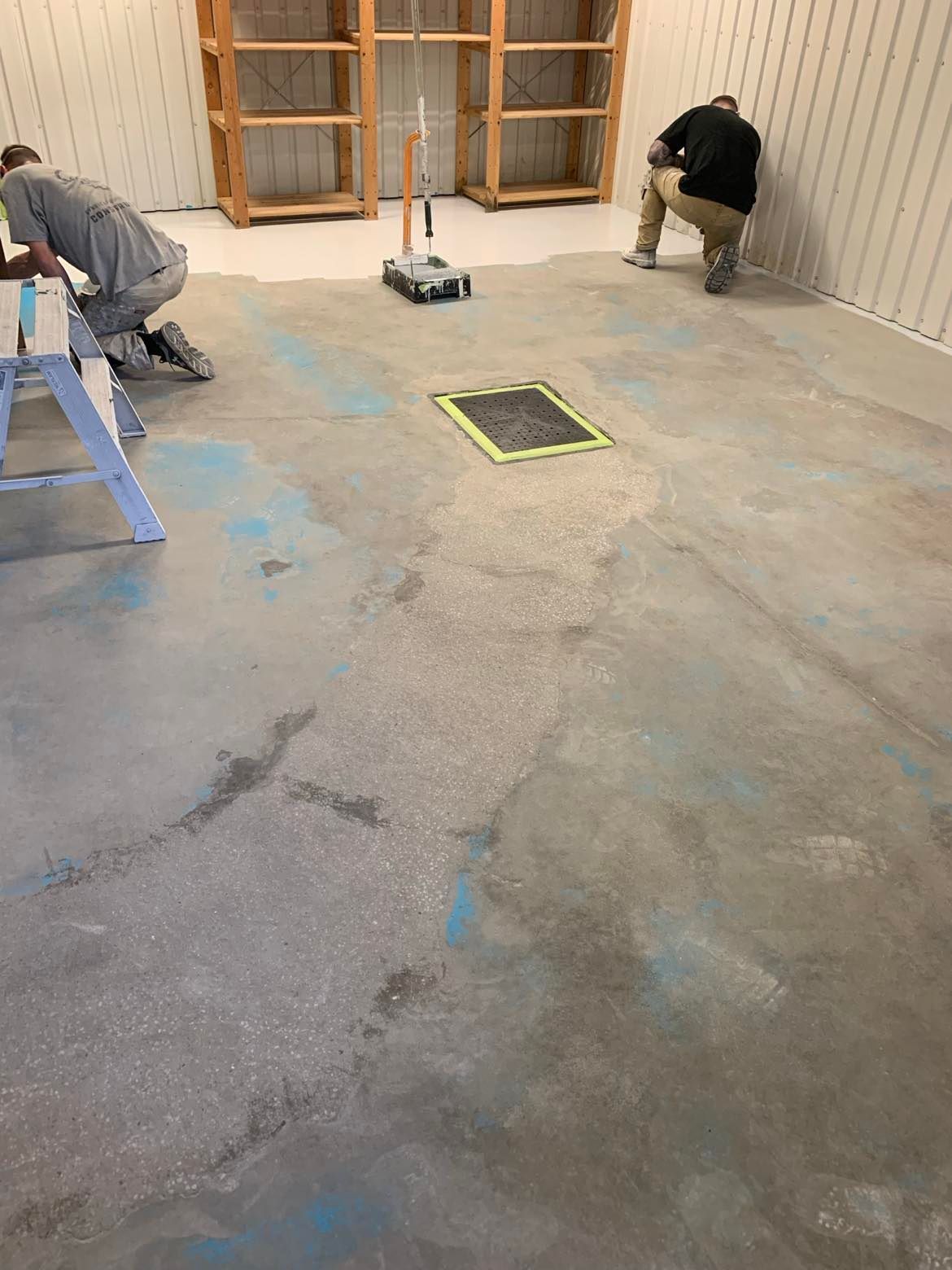 Two men are working on a concrete floor in a room.