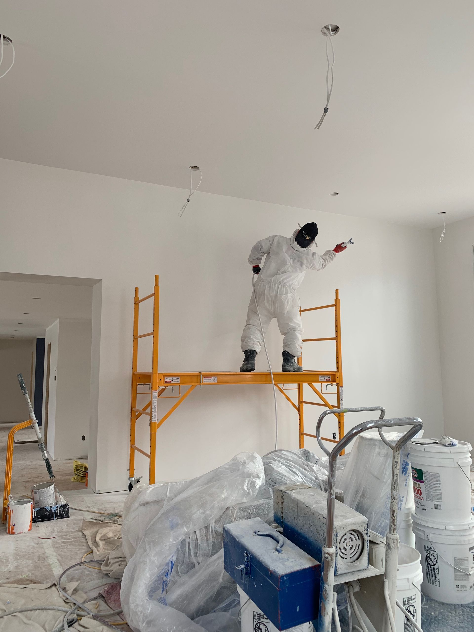 A man is standing on a scaffolding in a room painting a wall.