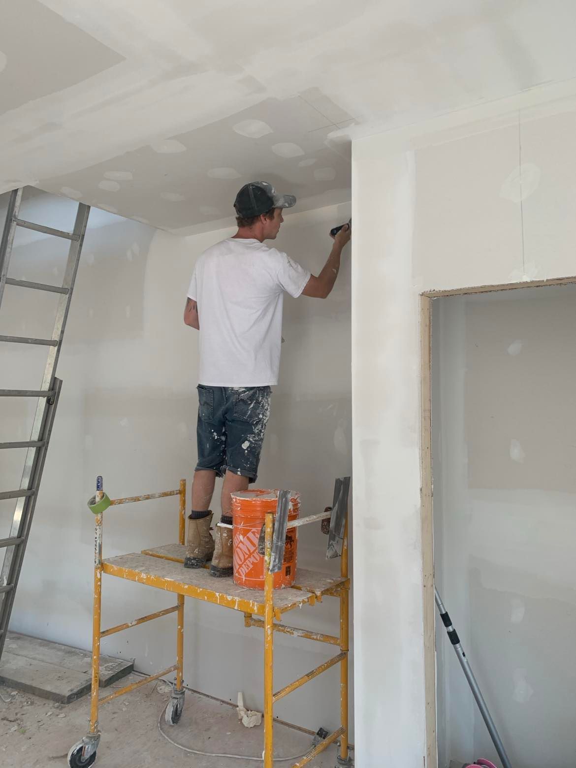A man is standing on a scaffolding painting a wall.