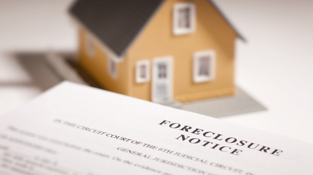 Foreclosure notice document with a small house model in the background.
