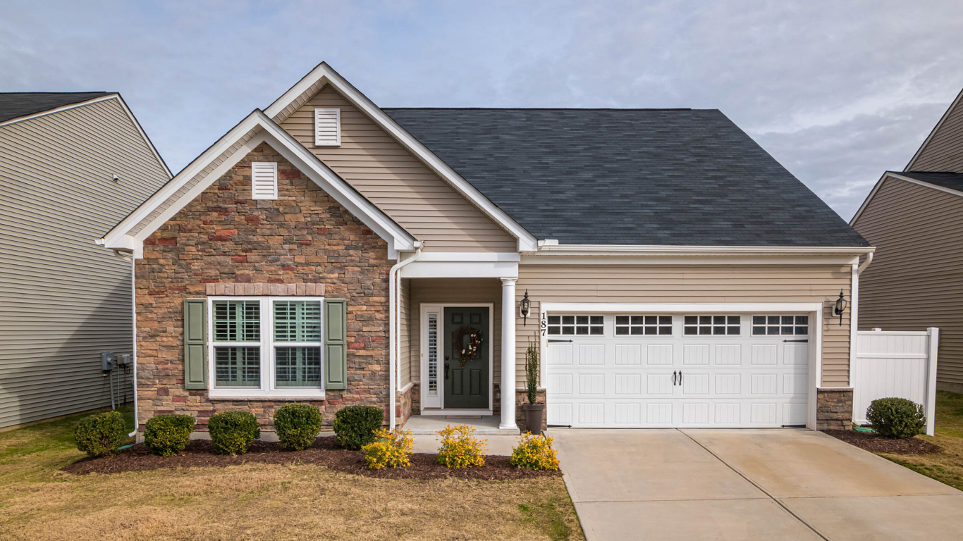 Tan and brown single-story house with a stone facade, white garage door, and green shutters.