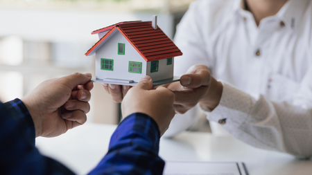 Two people exchanging a small house model, symbolizing a real estate transaction.