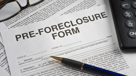 Pre-foreclosure form on a desk, next to a pen, calculator, and eyeglasses.