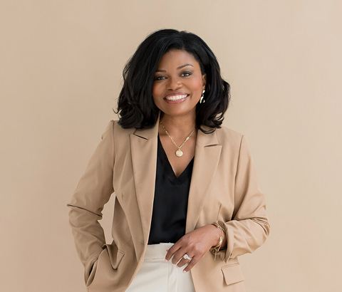 Smiling woman in a tan blazer and cream pants against a beige background
