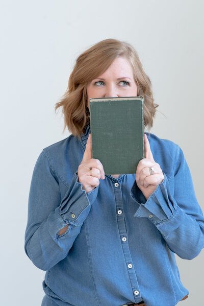 Person in a blue shirt holding a green notebook in front of their face