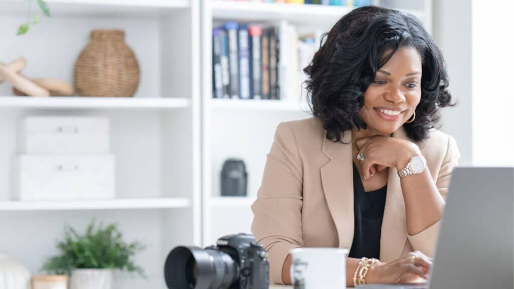 Woman smiling at desk with laptop and camera in a bright home office